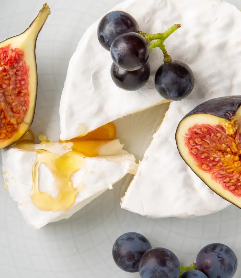 Sliced white cheese with figs and grapes on a light surface, drizzled with honey.