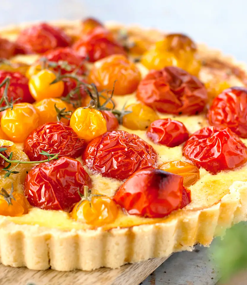 Roasted tomato tart with red and yellow cherry tomatoes on a pastry crust with herbs, displayed on a wooden surface.